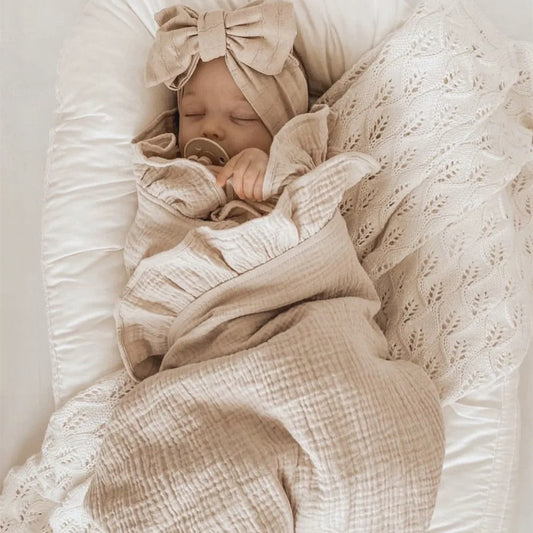Couverture d'Emmaillotage Beige en Mousseline de Coton sur un bébé dormant sur un lit blanc
